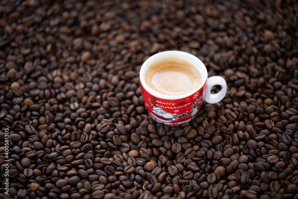 Flat lay with copy space, (selective focus) A Christmas cup with some creamy coffee is placed on some roasted coffee beans. Flat lay with copy space, (selective focus) A Christmas cup with some creamy coffee is placed on some roasted coffee beans.