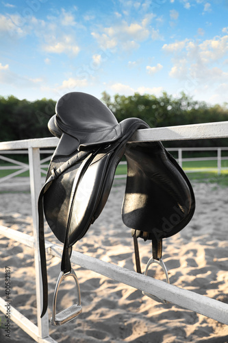Leather horse saddle on wooden fence outdoors