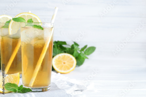 Delicious iced tea with lemon and mint on white wooden table. Space for text