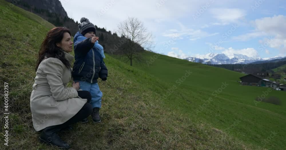 Mother and Child Enjoy Watching at Scenic Mountains. Tourist Travel in Picturesque Swiss Alps. Green Grass Pastures Meadows. Cottages in Village. Switzerland Europe Mother and Child Enjoy Watching at Scenic Mountains. Tourist Travel in Picturesque Swiss Alps. Green Grass Pastures Meadows. Cottages in Village. Switzerland Europe