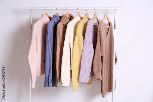 Warm sweaters hanging on rack against white background