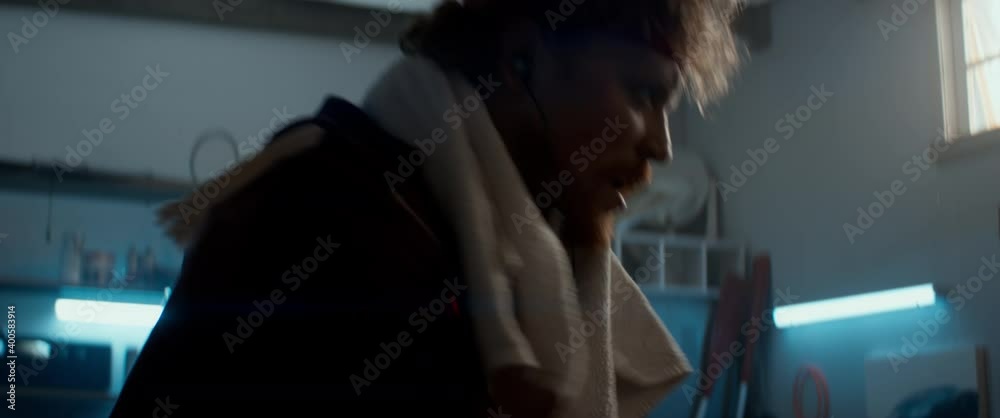 HANDHELD Portrait of unny determined overweight man in retro outfit cycling and sweating on a stationary bicycle in his home garage. Exercising during COVID-19 self isolation quarantine