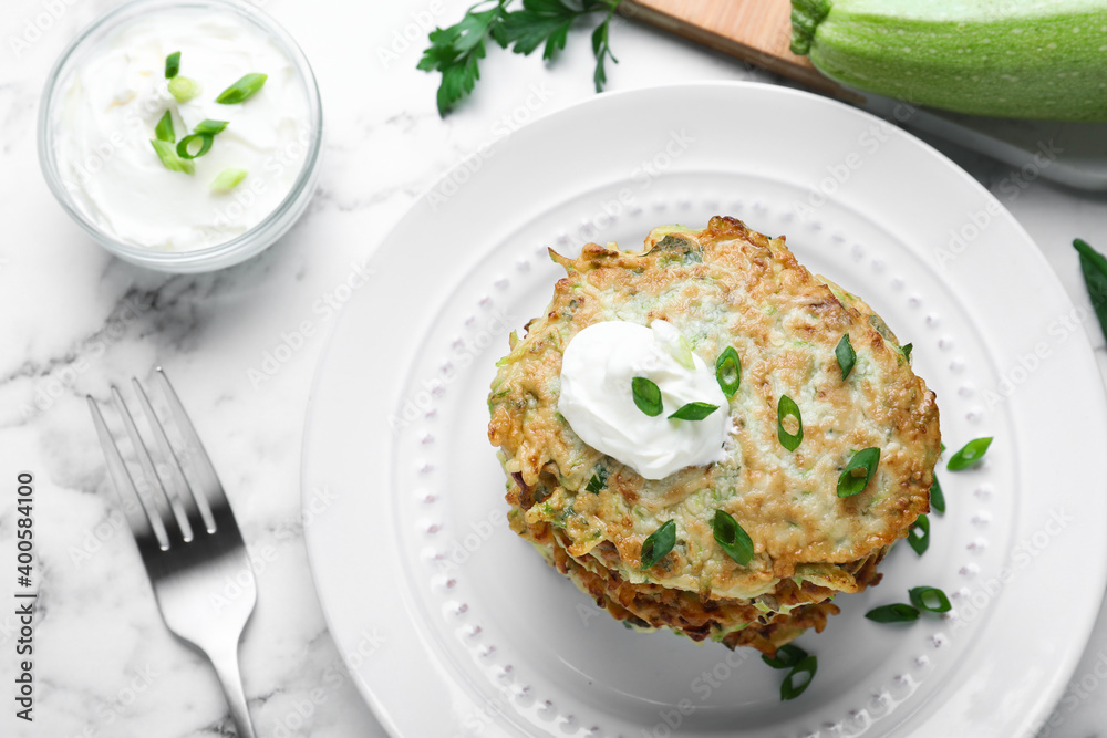 Delicious zucchini fritters served on white marble table, flat lay