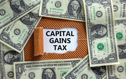 Capital gains tax symbol. The text 'Capital gains tax' appearing behind torn brown paper. Dollar bills. Business and capital gains tax concept.
