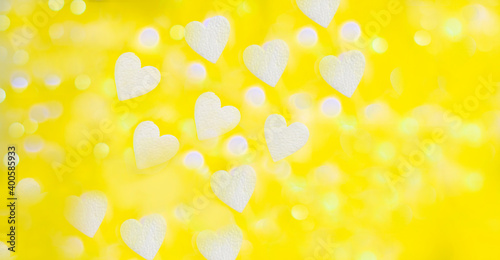 yellow background with bokeh of white foam hearts and light from a garland in partial blur,