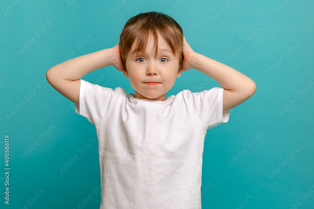 stylish child of four or five years old and holding his hands to his face he is surprised on a green background. Emotional boy posing for the camera stylish child of four or five years old and holding his hands to his face he is surprised on a green background. Emotional boy posing for the camera