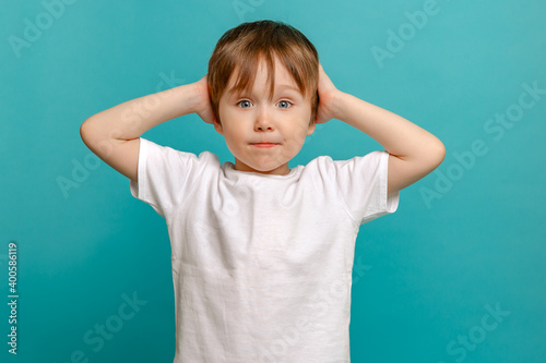 stylish child of four or five years old and holding his hands to his face he is surprised on a green background. Emotional boy posing for the camera