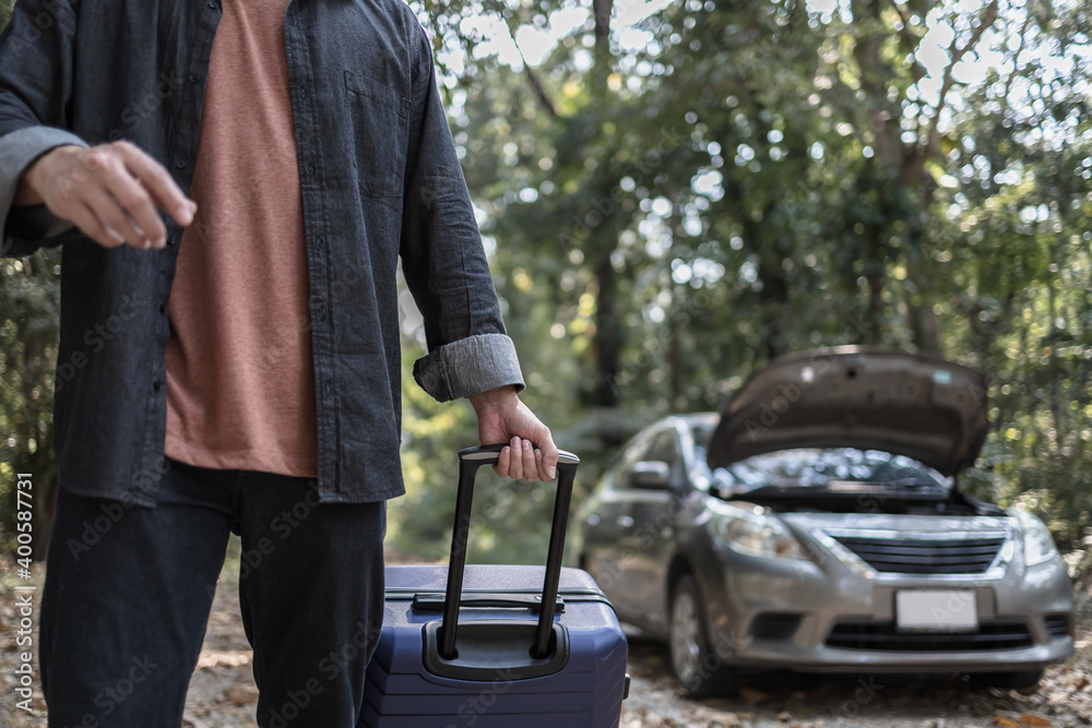Obraz premium Man' hand drag to travel bag in front of open hood of a broken car on the road in the forest. Car breakdown concept.