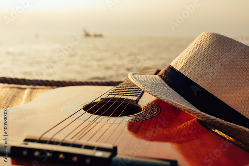 Fototapeta Naklejka Na Ścianę i Meble -  Guitar and hat on reed mat near the sea at sunset. Travel, vocation, holiday, summer concept.