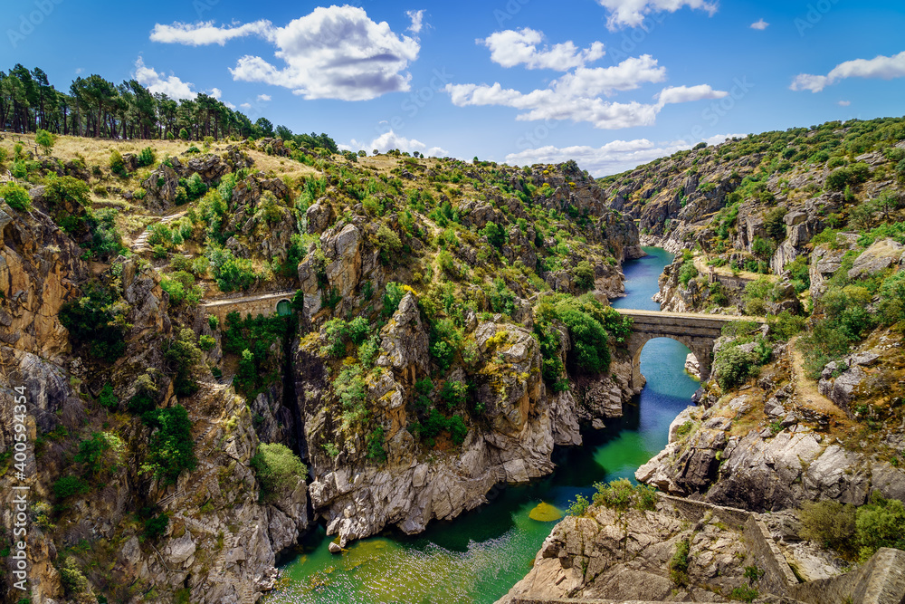 Atazar Madrid reservoir canyon with river of water and stone bridge across the river.
