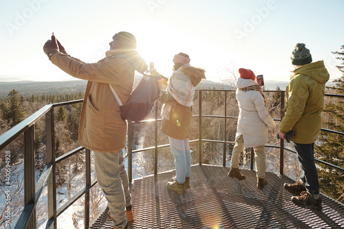Group of young friends in winterwear taking photo of mountains and forest