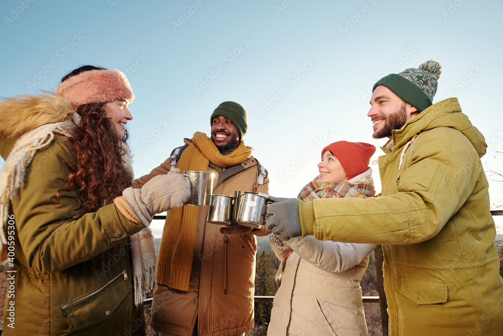 Happy young friends in winterwear cheering up with hot tea and chatting