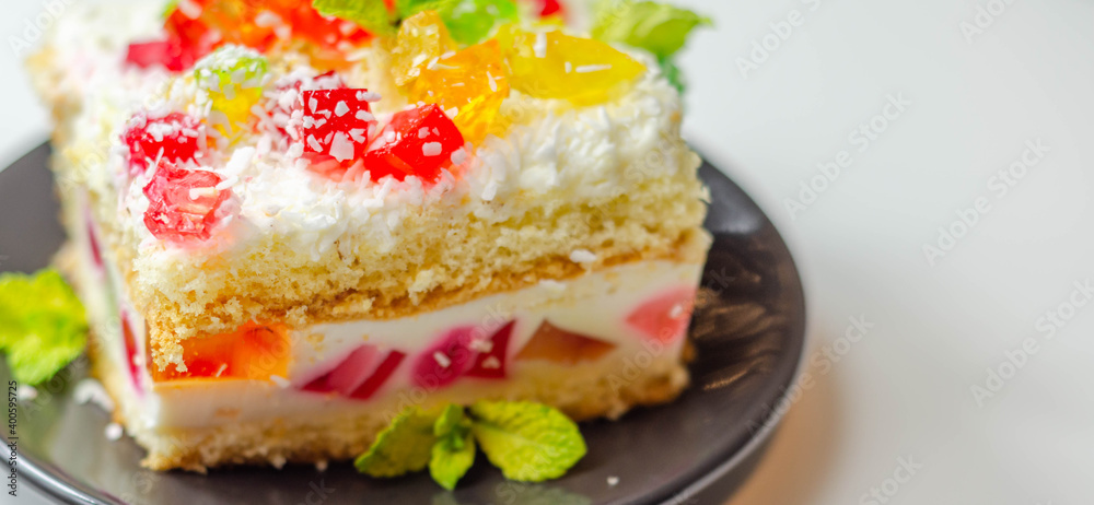 A portion of cream cake with pieces of colorful jelly and sprinkled with coconut flakes A portion of cream cake with pieces of colorful jelly and sprinkled with coconut flakes