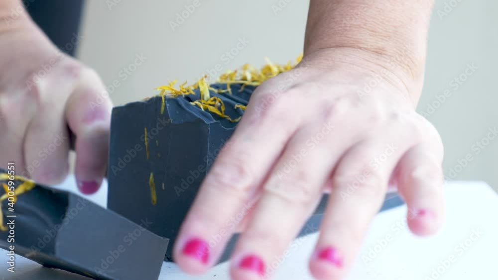 A women gently slices a newly made block of black handmade soap with a sharp knife