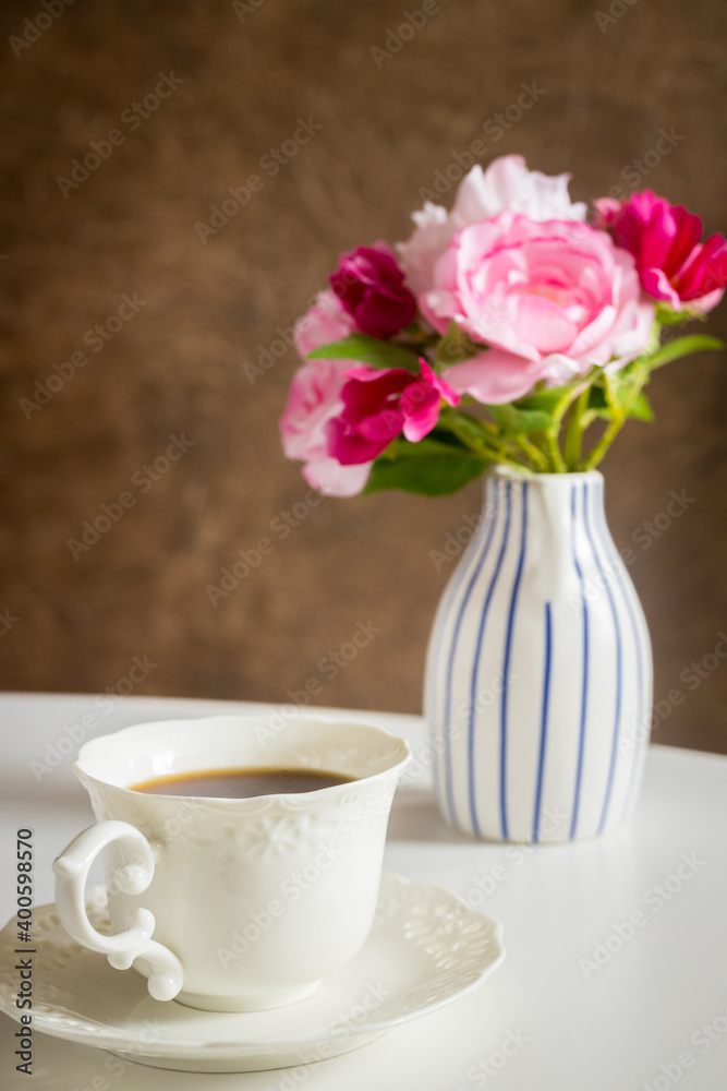 A cup of hot tea on the table behind it a stylish jug with a bouquet of flowers A cup of hot tea on the table behind it a stylish jug with a bouquet of flowers