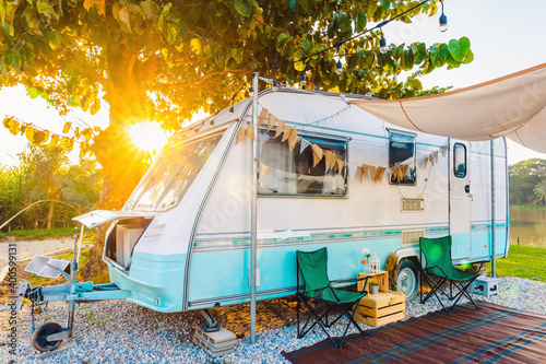 Foto Camping chairs placed outside cozy retro travel trailer Caravan under tree before sunset near the river in peaceful countryside