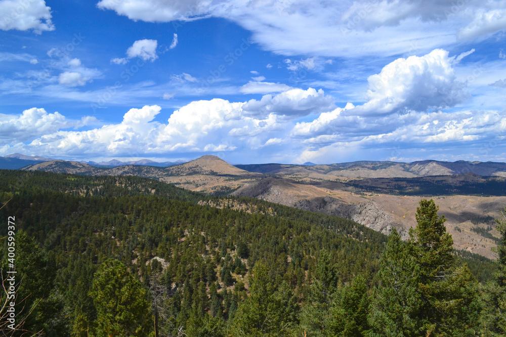 Scenic pass overlooking Colorado mountains and green pines with blue skies and wispy clouds.