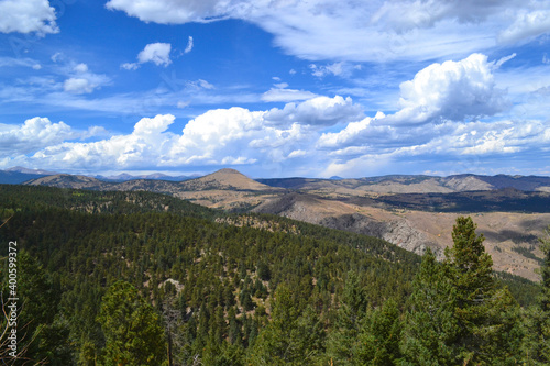 Scenic pass overlooking Colorado mountains and green pines with blue skies and wispy clouds.