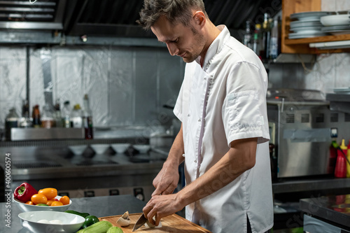 Young professional chef of modern restaurant in uniform cutting vegetables photo