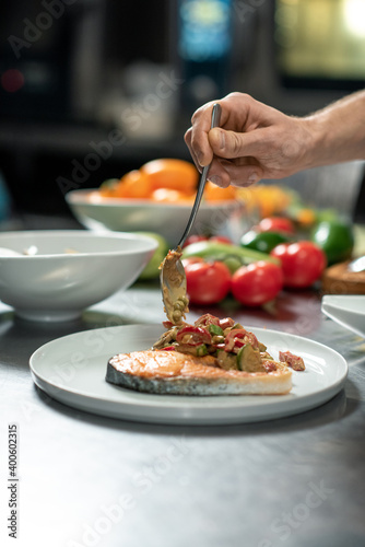 Hand of male chef putting hot appetizing vegetable stew on plate with salmon