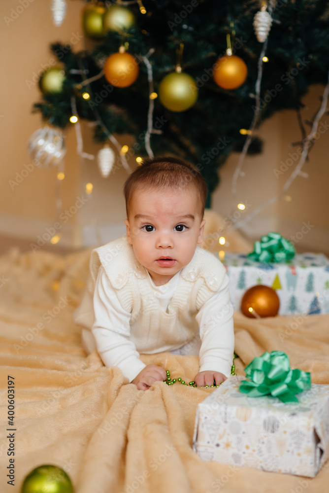 Cute smiling baby is lying under a festive Christmas tree and playing with gifts. Christmas and New Year celebrations Cute smiling baby is lying under a festive Christmas tree and playing with gifts. Christmas and New Year celebrations