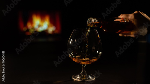 Close-up of a female hand with a glass of brandy on the background of the fireplace