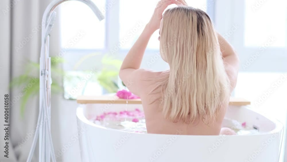 Beautiful Sexy Caucasian Blonde Girl In Bikini Lying In Flower Bath In Resort Day Spa Salon. Skin Care Therapy. Concept young woman relaxing in the bathtube. Slow motion video. stock footage Beautiful Sexy Caucasian Blonde Girl In Bikini Lying In Flower Bath In Resort Day Spa Salon. Skin Care Therapy. Concept young woman relaxing in the bathtube. Slow motion video. stock footage