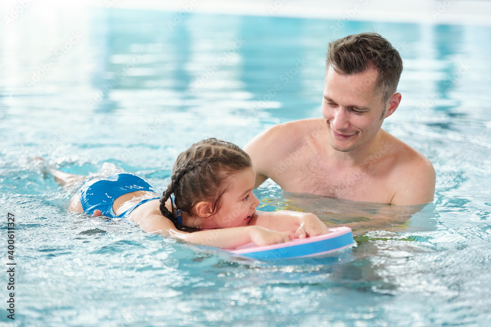 Happy young father teaching his little daughter to swim in pool in spa center Happy young father teaching his little daughter to swim in pool in spa center