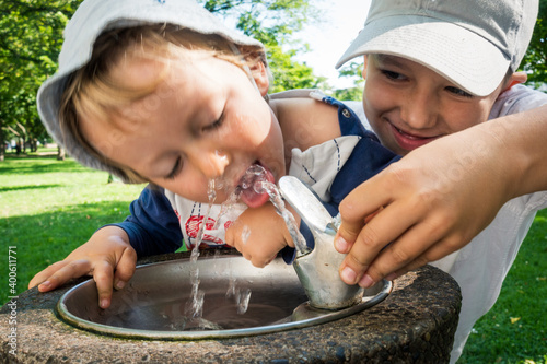 Little boy drinking tab water with the help of his brother