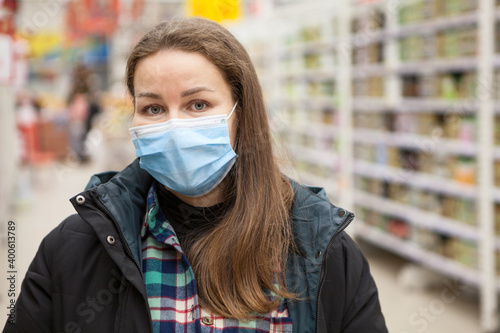 Wearing face mask in public places during the coronavirus pandemic, adult woman portrait against store shelves