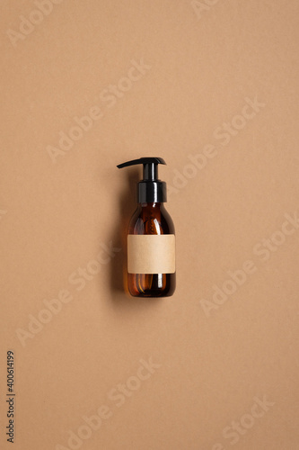 Amber glass pump bottle with blank label on brown table. Natural cosmetic product packaging design, branding. Flat lay, top view.