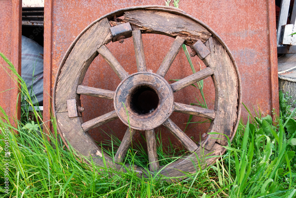 Old wooden wheel leaned on the rusty metal surface on the grass