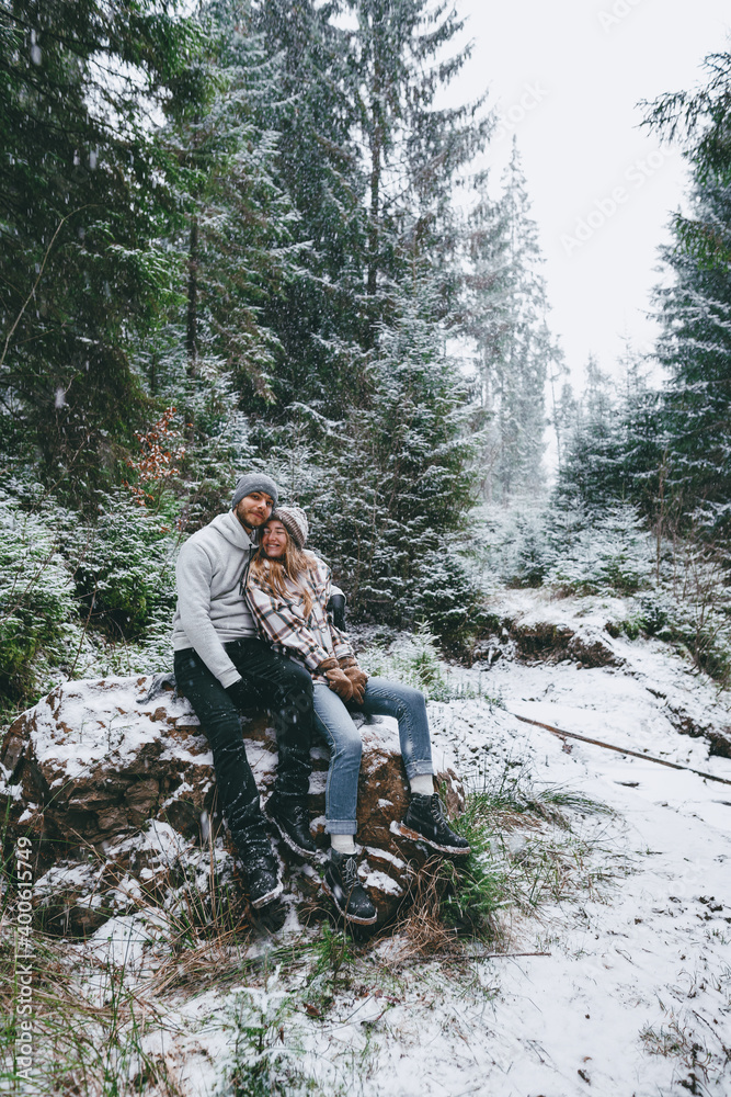 Happy Christmas couple sitting on rock in winter forest