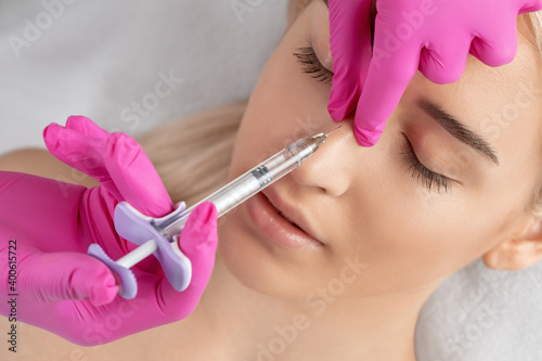 The doctor does injections to correct the hump on the nose with the beauty of the blonde. The beautician doees injections against wrinkles on the face. Women's cosmetology in a beauty salon.