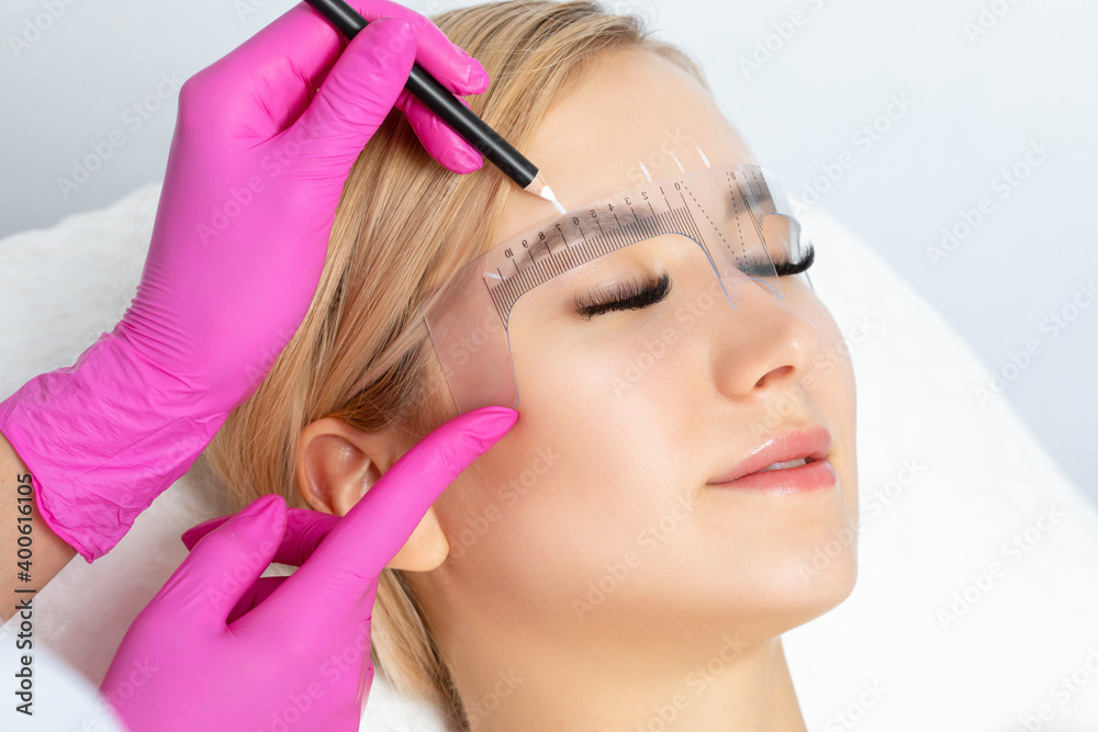 Permanent make-up for eyebrows of beautiful woman with thick brows in beauty salon. Closeup beautician doing tattooing eyebrow. Professional makeup and cosmetology skin care.