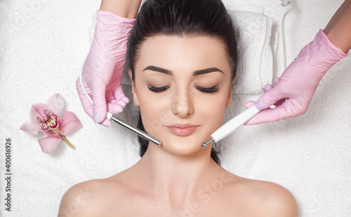 The cosmetologist makes the apparatus a procedure of Microcurrent therapy of a beautiful, young woman in a beauty salon. Cosmetology and professional skin care. photo