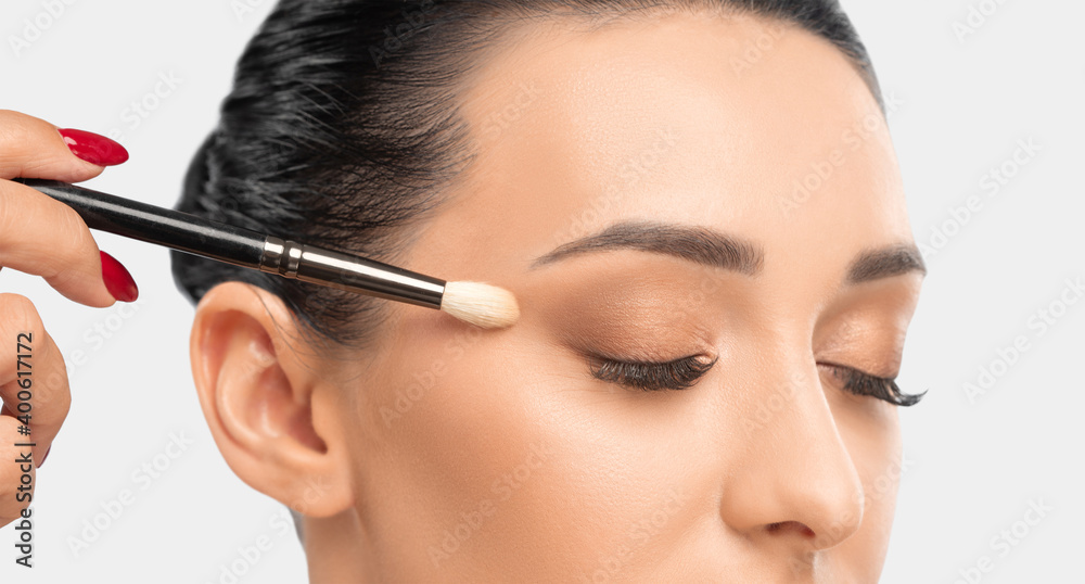 Portrait of a charming brunette woman with healthy clean skin. Makeup artist applies eye shadow.The concept of aesthetic cosmetology and makeup.