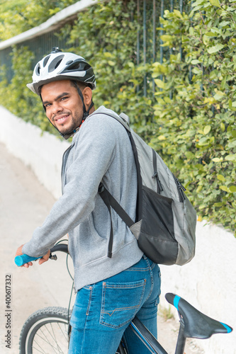 Young black man sitting on a bike in a park, leaning on the handlebars smiling, side view