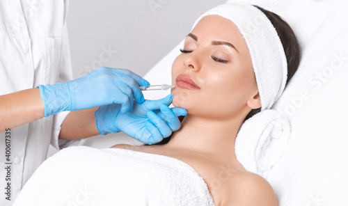 Cosmetologist does injections for lips augmentation and anti wrinkle in the nasolabial folds of a beautiful woman. Women s cosmetology in the beauty salon.