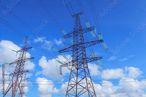 High voltage lines and power pylons with cirrus clouds in the blue sky.