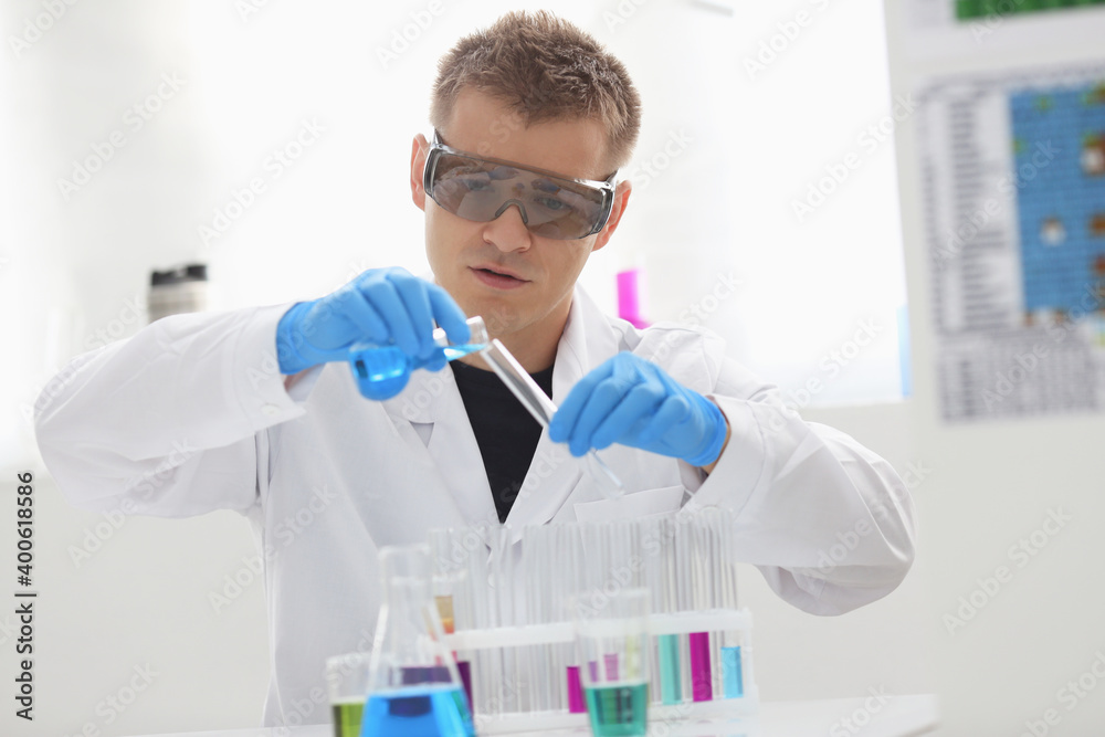 A male chemist holds test tube of glass in his hand overflows a liquid solution of potassium permanganate conducts an analysis reaction takes various versions of reagents using chemical manufacturing A male chemist holds test tube of glass in his hand overflows a liquid solution of potassium permanganate conducts an analysis reaction takes various versions of reagents using chemical manufacturing