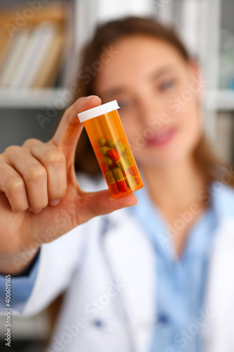 Beautiful smiling female doctor hold in arms pill bottle and offer it to visitor closeup. Panacea or life save antidepressant from legal store prescribe vitamin medic aid for healthy lifestyle