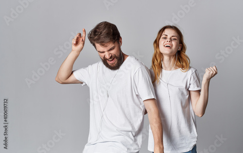 cheerful man and woman in headphones listen to music and dance on a gray background