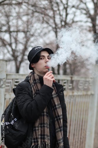 Young pale guy in a coat is holding an umbrella. It's winter outside, it's gray and cold. But style, beauty and acting make a photo into a mysterious picture.