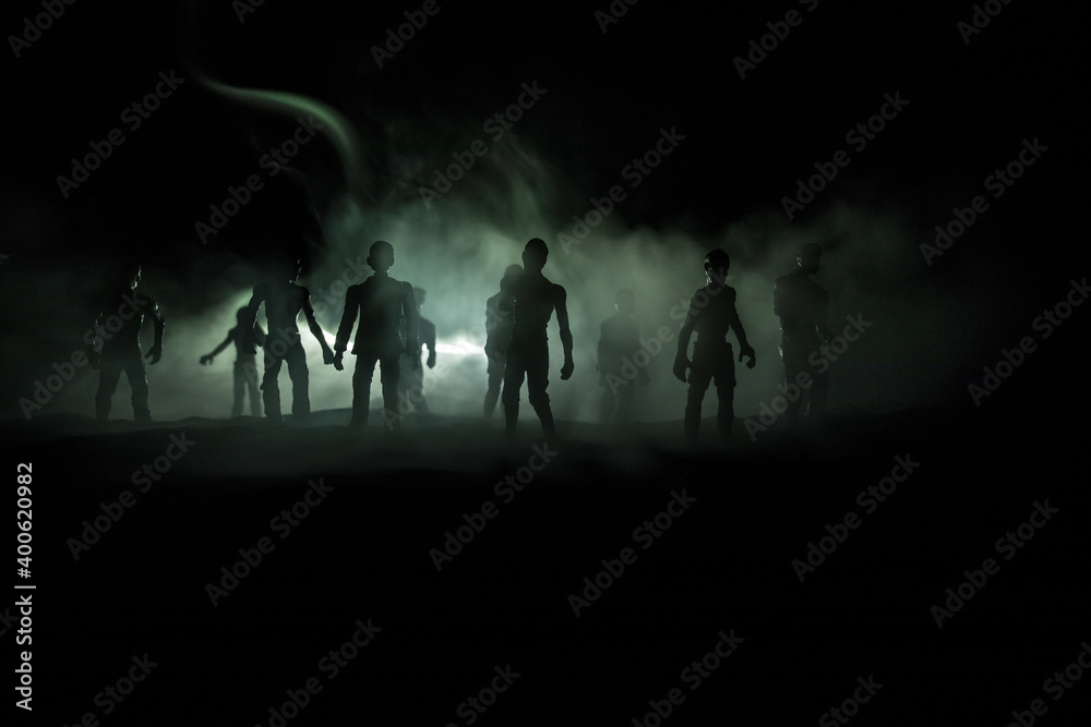 Fototapeta premium Scary view of zombies at cemetery dead tree, moon, church and spooky cloudy sky with fog, Horror Halloween concept with glowing pumpkin. Selective focus