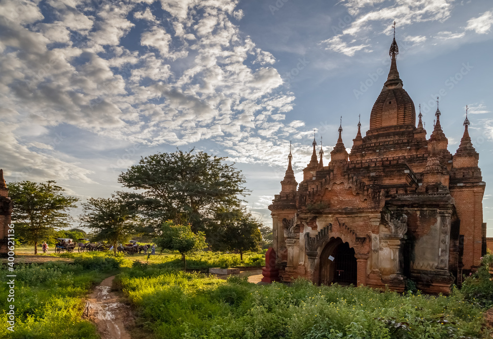 Ancient Buddhist pagoda against cloudy sky in the old city of Bagan, the world heritage site in Myanmar (Burma). Carriages with tourists in the background.