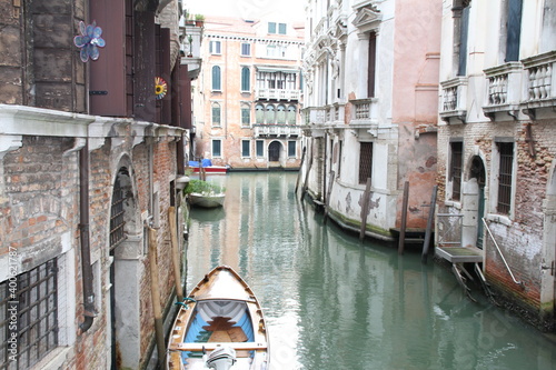 narrow water canal in Venice, green water between the buildings of Venetian tenement houses and boats moored close to the walls