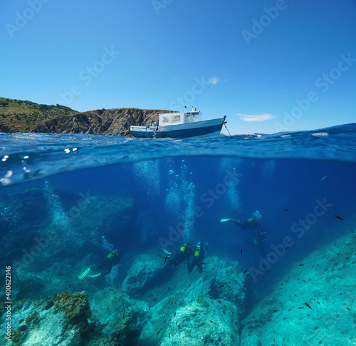 Scuba diving, a boat on the surface and scuba divers underwater, Mediterranean sea, split view over and under water, Marine reserve of Cerbere Banyuls, France, Occitanie
