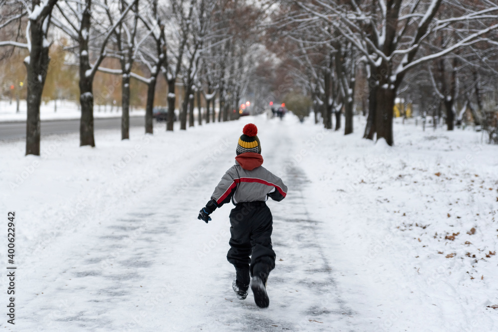 Boy runs through the park in winter. Back view. Child walks in snowy park.