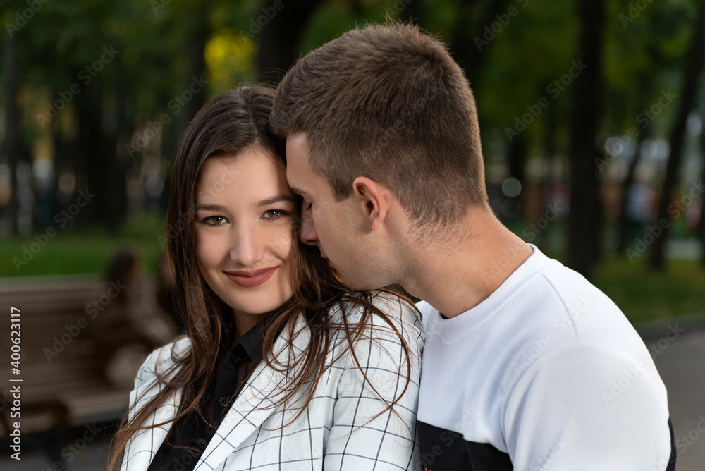 Portrait of beautiful young couple in park. Guy gently touches the girls cheek with his nose.
